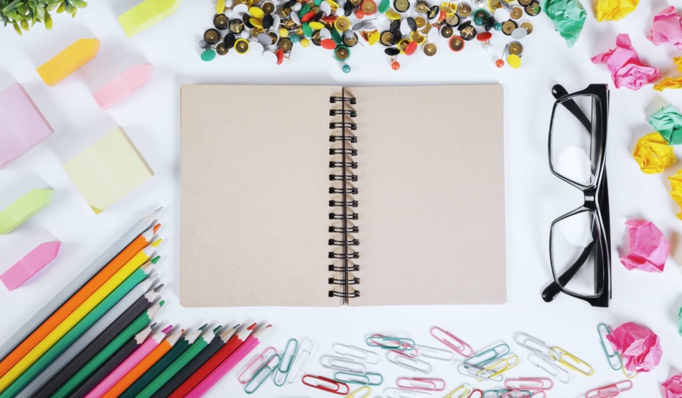 Close up of modern office desktop with blank notepad and other supplies. Above view. Mock up